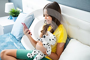 Teenager girl relax on bed at home using phone, browse internet on smartphone. Happy teen girl with toy, positive and