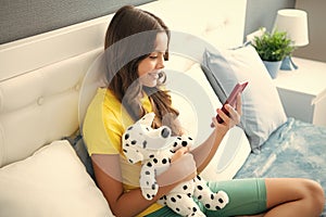 Teenager girl relax on bed at home using phone, browse internet on smartphone. Happy teen girl with toy, positive and