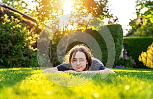 Teenager girl relaxing lying on green grass in garden backyard at sunset with backlit.