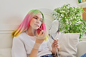 Teenager girl sitting at home on bed with make-up mirror painting her lips with lip gloss