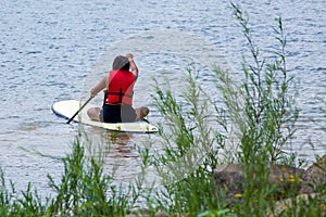 A teenager girl sitting on a paddle board.