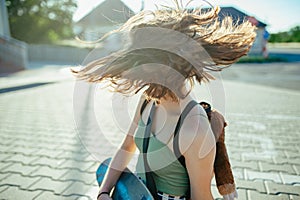 Teenager girl with skateboard spending time outdoors in city during warm summer holiday day. Flying hair, spinning head.