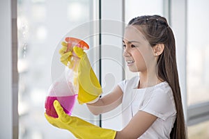 Teenager girl splashing cleanser on the window.