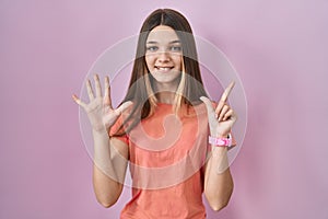 Teenager girl standing over pink background showing and pointing up with fingers number seven while smiling confident and happy