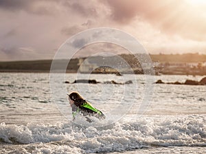 Teenager girl on a surf board in a waves. Blackrock diving tower in the background. Beautiful cloudy sky, Galway city, Ireland.