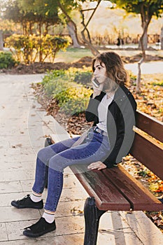 Teenager girl taking by phone on the bench in autumn park