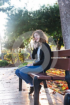 Teenager girl taking by phone on the bench in autumn park