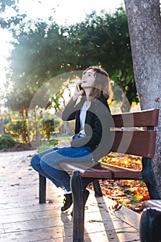 Teenager girl taking by phone on the bench in autumn park