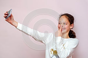 Teenager girl taking selfie with her cell phone on pink background.