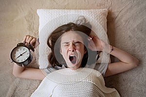 Teenager girl turning alarm off in the morning while lying in bed