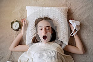 Teenager girl turning alarm off in the morning while lying in bed