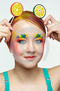 Teenager girl with unusual face art make-up . Child with lollipops in hands on head like ears