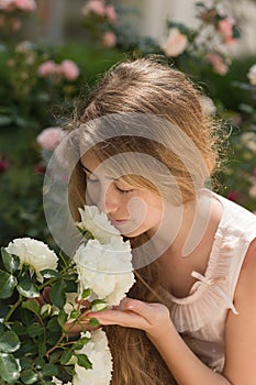 Teenager girl with waivy blonde hair smelling white garden roses