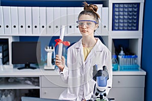 Teenager girl working at scientist laboratory holding degree thinking attitude and sober expression looking self confident