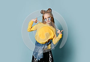 Teenager girl in yellow sweatshirt and black skirt poses as a top model pointing fingers at herself with both hands