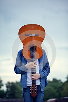 Teenager with a guitar instead of a head in the park. Crazy and cool young man with a guitar