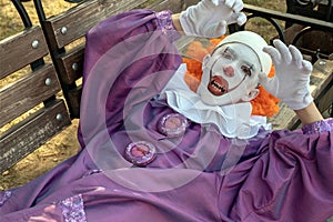 A teenager guy in a clown costume with sharp teeth lies on a bench. Street make-up, Halloween cosplay or a horror character