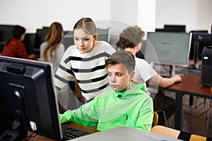 Teenager guy helps girl solve problem on computer in school class