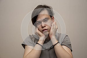 A teenager in handcuffs sits on a gray background, medium plan. Juvenile delinquent, criminal liability of minors.