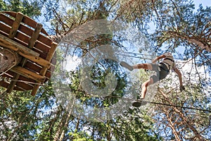 Teenager having fun on high ropes course, adventure park, climbing trees in a forest in summer