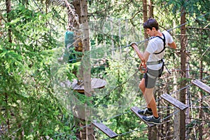 Teenager having fun on high ropes course, adventure park, climbing trees in a forest in summer