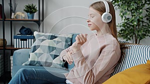 Teenager in headphones enjoying music and dancing moving hands holding smartphone at home