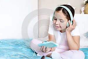 A teenager with headphones listening to music and holding a phone in his hands, she is in the bedroom on the bed. The