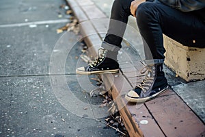 teenager in hightop sneakers sitting on a sidewalk curb