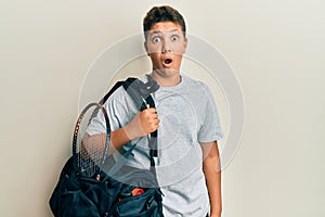 Teenager hispanic boy holding sport bag scared and amazed with open mouth for surprise, disbelief face