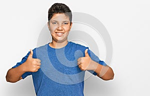 Teenager hispanic boy wearing casual clothes success sign doing positive gesture with hand, thumbs up smiling and happy