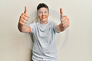 Teenager hispanic boy wearing casual grey t shirt approving doing positive gesture with hand, thumbs up smiling and happy for