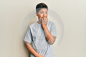 Teenager hispanic boy wearing casual grey t shirt looking stressed and nervous with hands on mouth biting nails