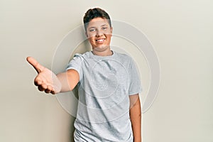 Teenager hispanic boy wearing casual grey t shirt smiling friendly offering handshake as greeting and welcoming