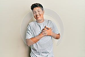 Teenager hispanic boy wearing casual grey t shirt smiling with hands on chest with closed eyes and grateful gesture on face