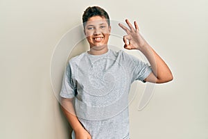 Teenager hispanic boy wearing casual grey t shirt smiling positive doing ok sign with hand and fingers