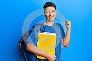 Teenager hispanic boy wearing school bag and holding books screaming proud, celebrating victory and success very excited with