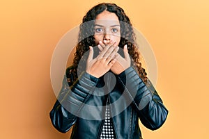 Teenager hispanic girl wearing black leather jacket shocked covering mouth with hands for mistake