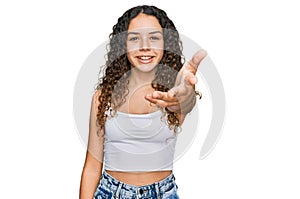 Teenager hispanic girl wearing casual clothes smiling friendly offering handshake as greeting and welcoming