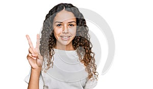 Teenager hispanic girl wearing casual white t shirt smiling with happy face winking at the camera doing victory sign