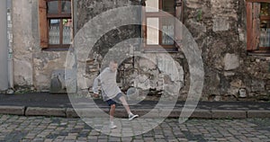 Teenager kid kicking soccer ball with feet. Young boy football player practicing tricks at old city street. Old damaged