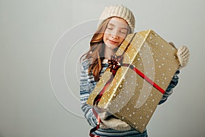 The teenager in a knitted hat, sweater and gloves closed her eyes in pleasure. A girl hugs her Christmas present from