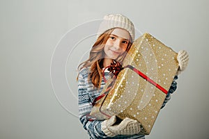 Teenager in a knitted hat, sweater and gloves. A girl hugs her Christmas present from her parents. Her friends