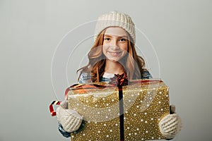 A teenager in a knitted hat, sweater and gloves is smiling. A girl hugs her Christmas present from her parents. She was