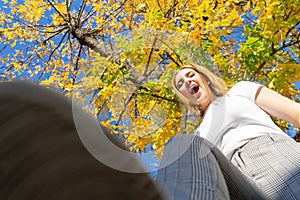 Teenager laughing steeping the camera on a fight with her shoes with a autumn leaves tree