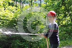 Teenager learning the firefighter profession. The girl in fire helmet pours water from the hose