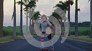 A teenager with long hair rides a skateboard along a beautiful road with palm trees. Los Angeles. Boy longboarder riding