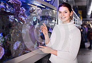 teenager looking at colored tropical fishes and underwater rocks into big aquarium