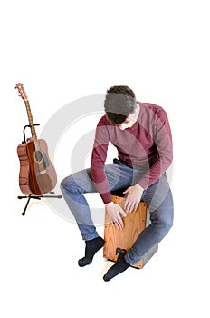 Teenager man musician sit on a cajon and play with a guitar in b