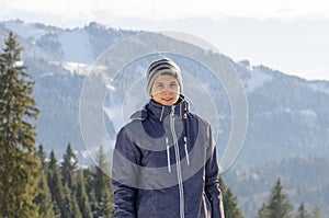 Teenager man smiling in winter jacket at mountains with ski slop