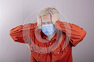 A teenager in a medical mask holds his head with his hands. Concept: headache, symptoms of coronavirus disease,